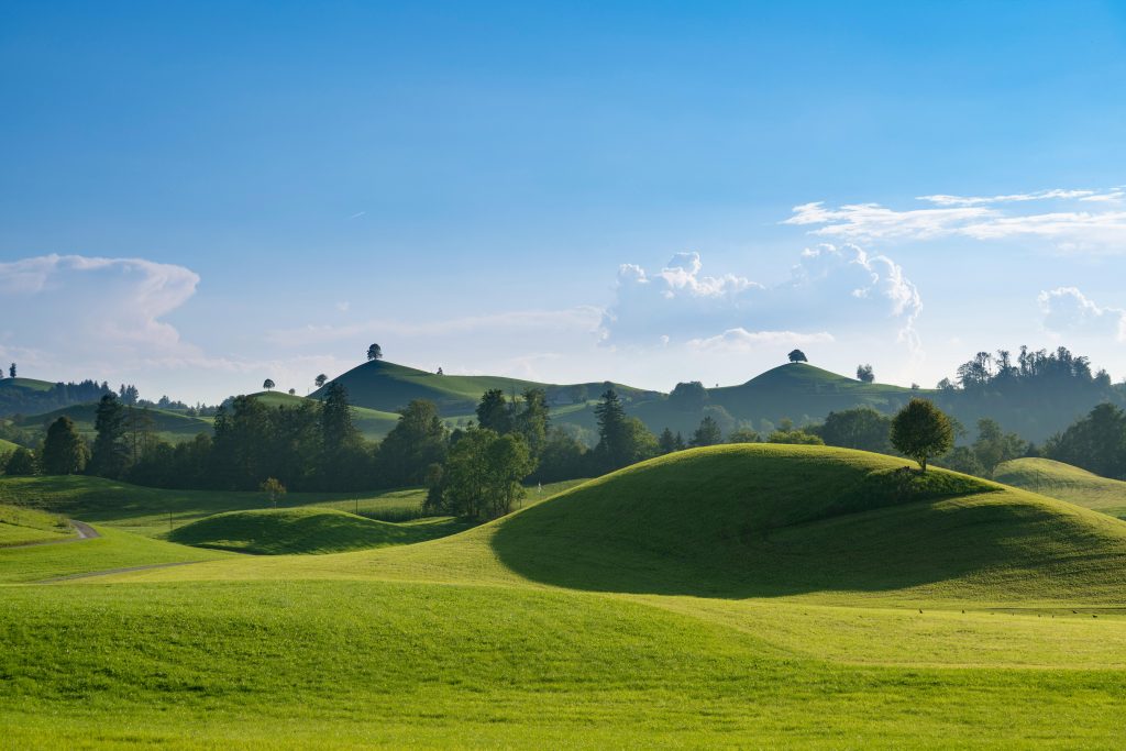 Peaceful landscape of rolling green hills under a vibrant blue sky with clouds.